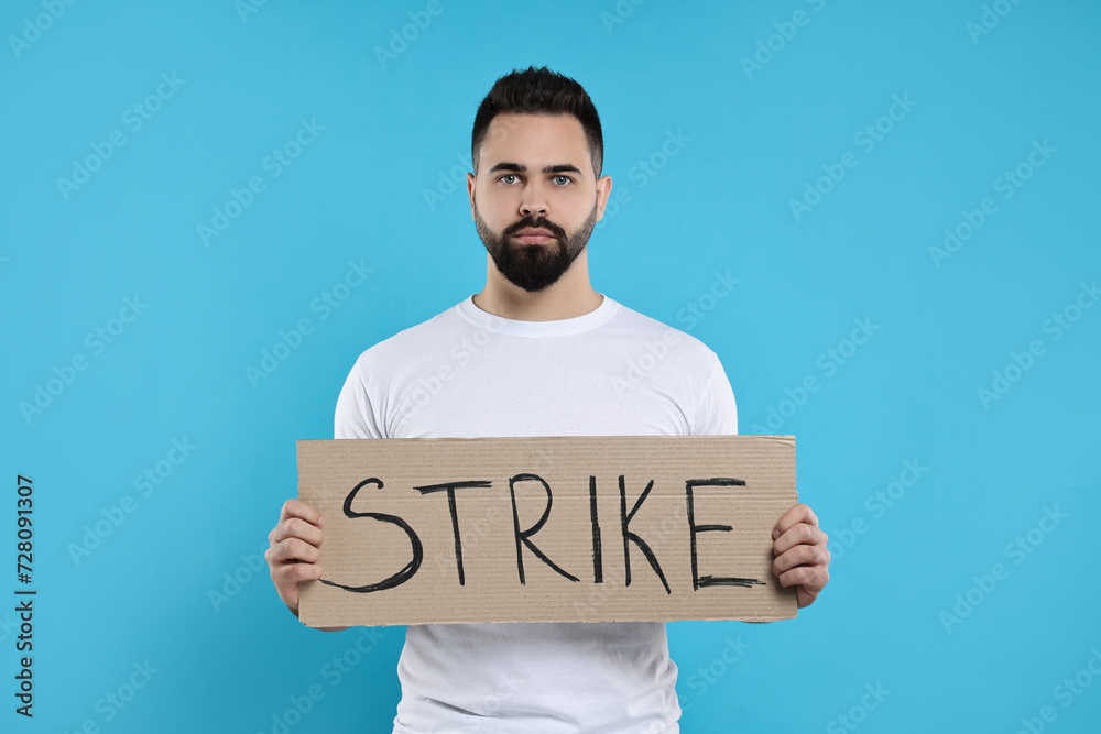 Man holding cardboard banner with word Strike on light blue background Man holding cardboard banner with word Strike on light blue background