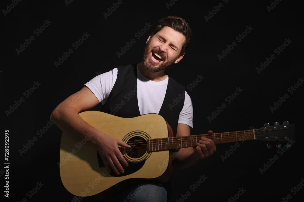 Obraz premium Handsome man with acoustic guitar singing while woman holding microphone on dark background, closeup