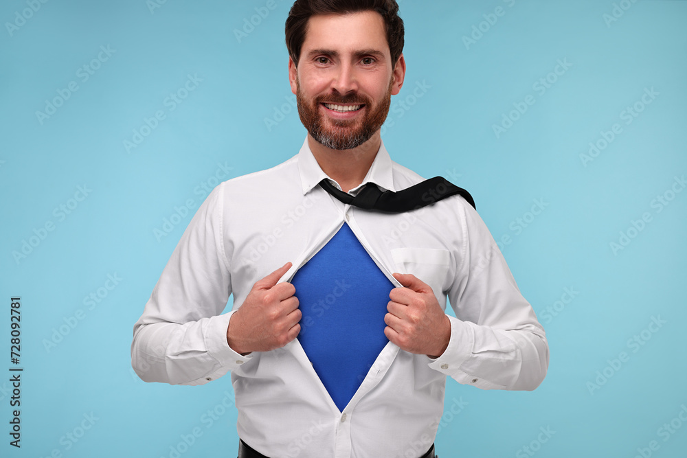 Happy businessman wearing superhero costume under suit on light blue background Happy businessman wearing superhero costume under suit on light blue background