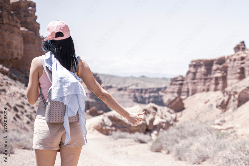 Naklejka premium girl in the canyon traveling through the canyon with a phone and a backpack in the summer at sunset