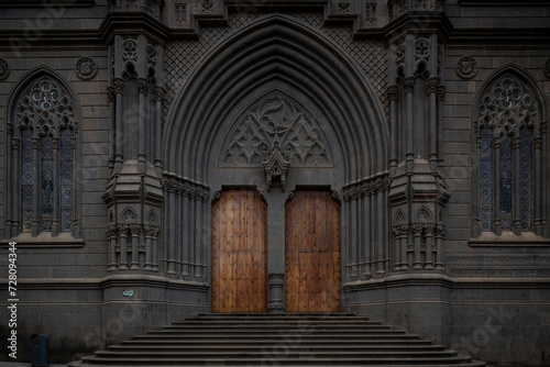 SPAIN, Gran Canaria, Arucas: Vertical View of Neo-Gothic religious architecture charm in the stone facade of San Juan Bautista Church, entrance doors to historic architectural gem in the heart of town photo