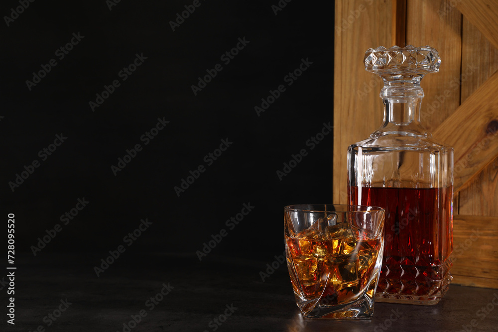 Whiskey in glass and bottle near wooden crate on dark table against black background. Space for text Whiskey in glass and bottle near wooden crate on dark table against black background. Space for text