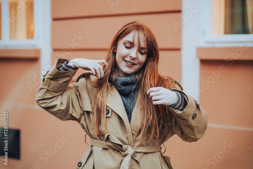 A chic red hair lady in warm outfit is touching her hair outside.