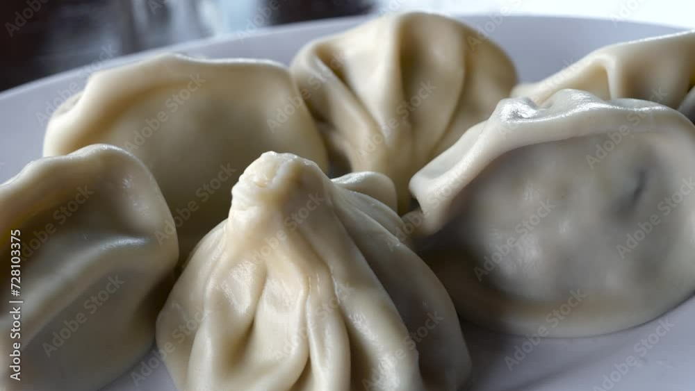 Traditional Georgian Khinkali dumplings are served on a white plate on the dining table, a close-up view shot. Traditional Georgian Khinkali dumplings are served on a white plate on the dining table, a close-up view shot.