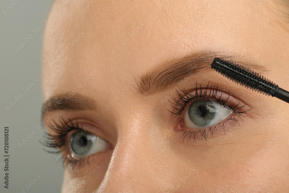 Fototapeta premium Woman applying mascara on grey background, closeup