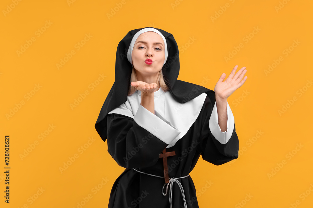 Woman in nun habit blowing kiss against orange background Woman in nun habit blowing kiss against orange background
