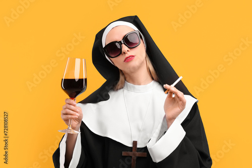 Woman in nun habit holding glass of wine and cigarette against orange background photo