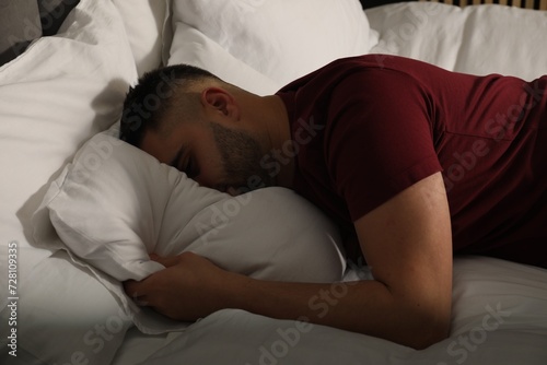 Sad man hiding face in pillow on bed at home