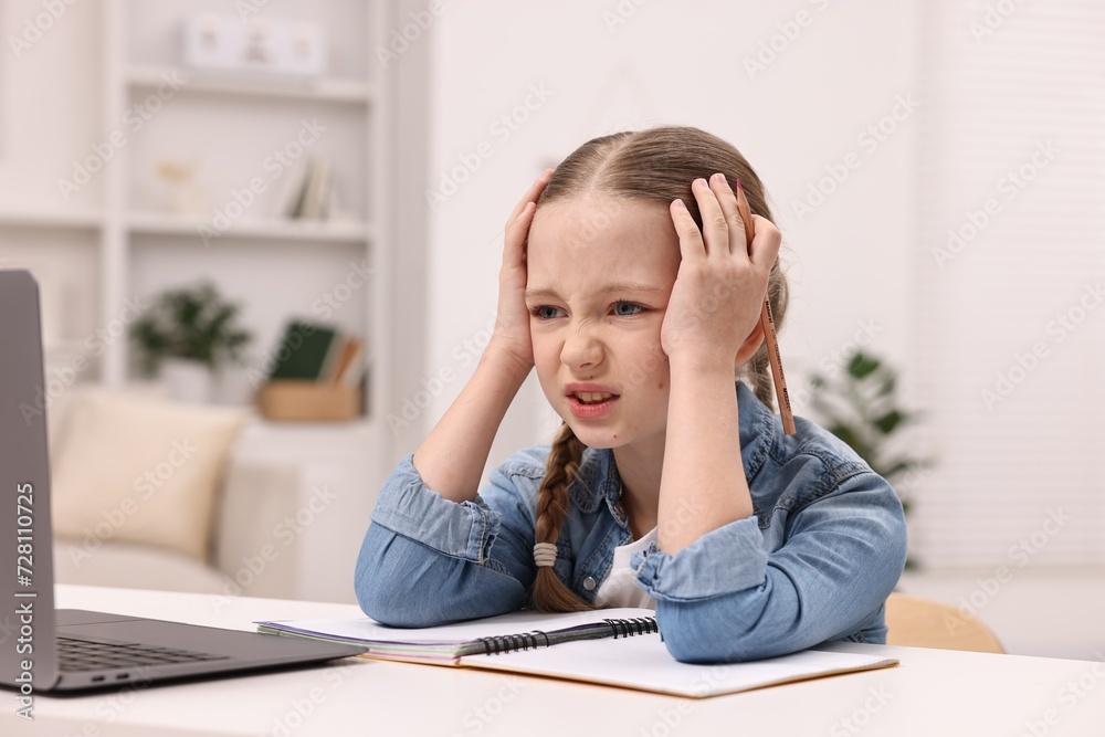Little girl suffering from headache while doing homework at home Little girl suffering from headache while doing homework at home