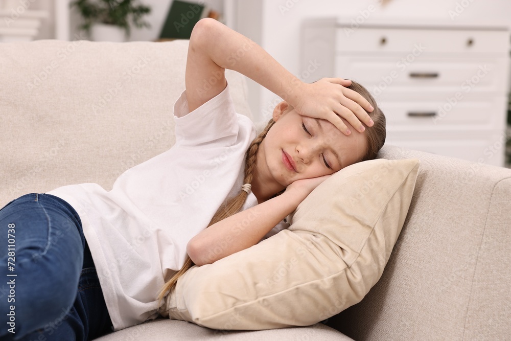 Little girl suffering from headache on sofa indoors