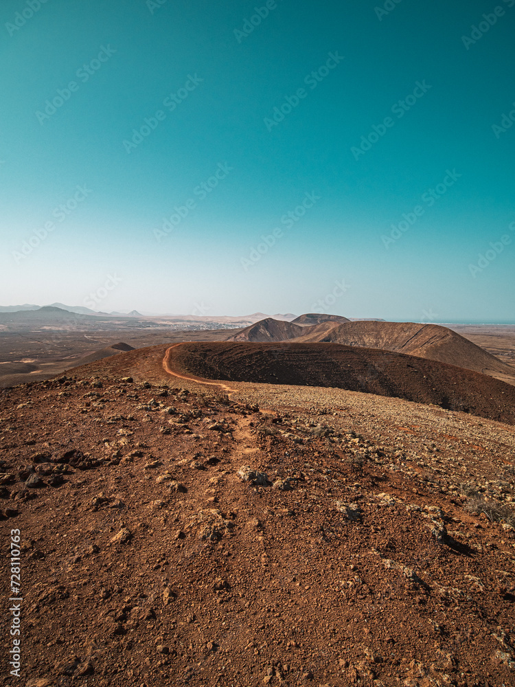 Volcanic desert landscape with mountains and the ocean visible in the background.