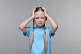 Little girl suffering from headache on grey background