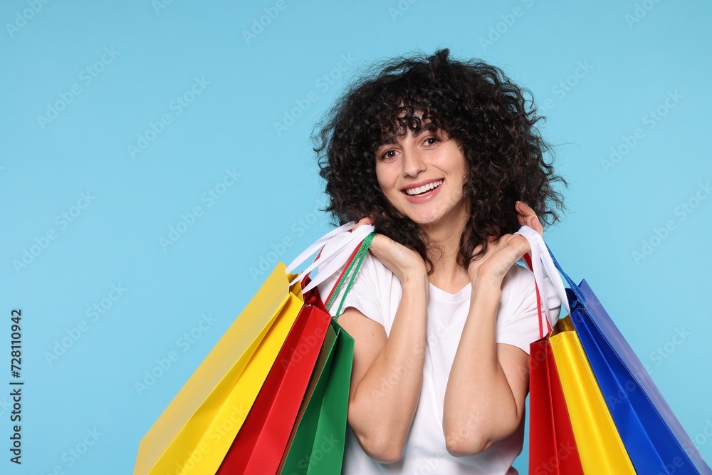 Happy young woman with shopping bags on light blue background Happy young woman with shopping bags on light blue background