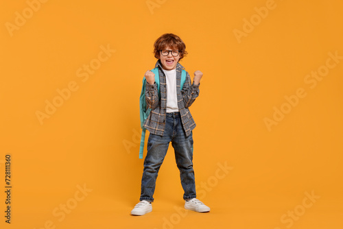 Emotional schoolboy with backpack on orange background