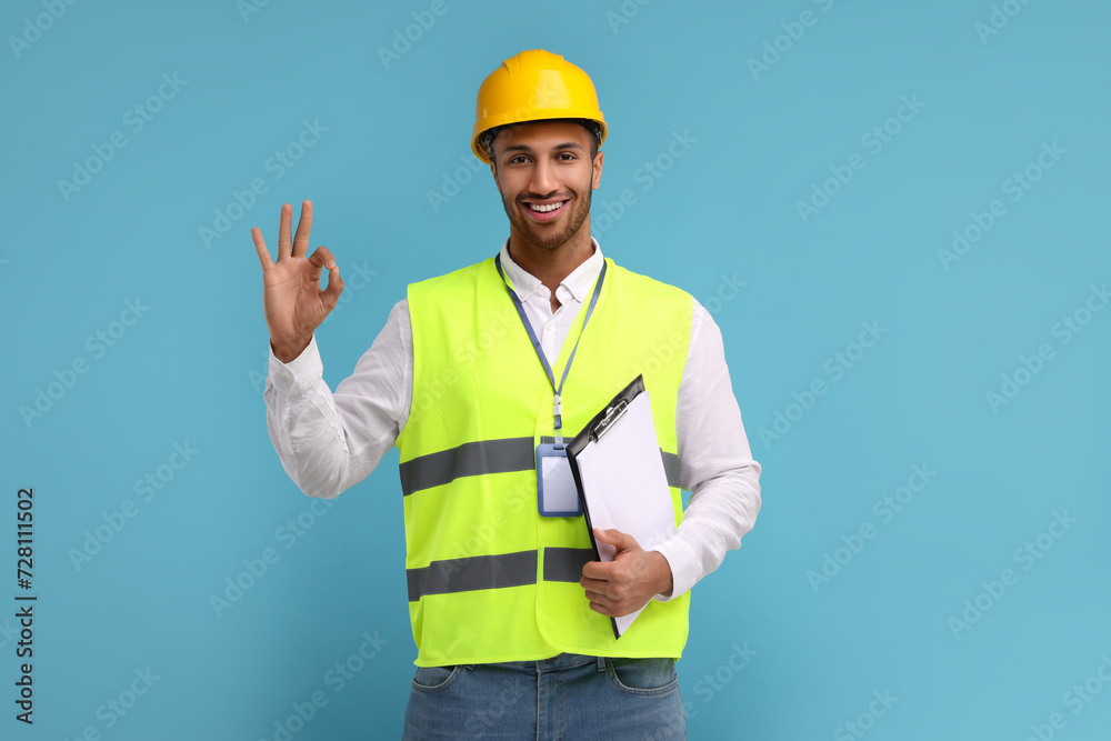 Engineer in hard hat showing ok gesture on light blue background Engineer in hard hat showing ok gesture on light blue background