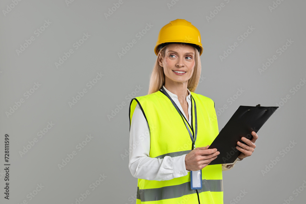 Engineer in hard hat holding clipboard on grey background, space for text Engineer in hard hat holding clipboard on grey background, space for text