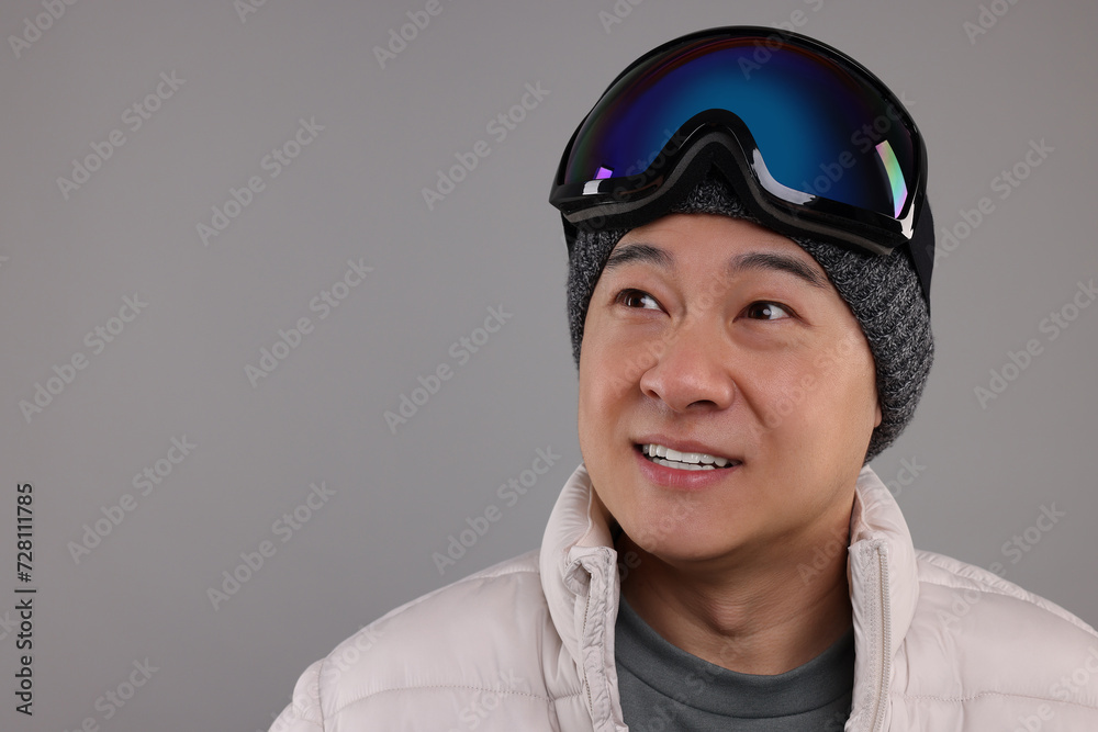 Winter sports. Happy man with ski goggles on grey background, space for text Winter sports. Happy man with ski goggles on grey background, space for text