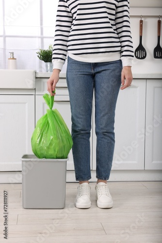 Woman taking garbage bag out of trash bin in kitchen, closeup