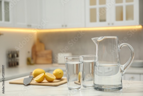 Jug  glasses with clear water and lemons on white table in kitchen
