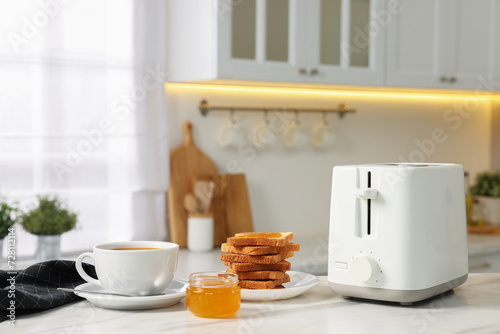 Breakfast served in kitchen. Toaster, crunchy bread, honey and coffee on white table