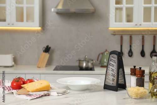 Grater, delicious cheese and other products on white marble table in kitchen