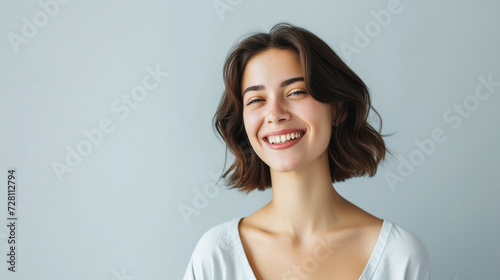 A joyful, prosperous woman dressed casually, beaming with confidence, standing against a light gray background. Her expression is one of satisfaction and self-confidence.