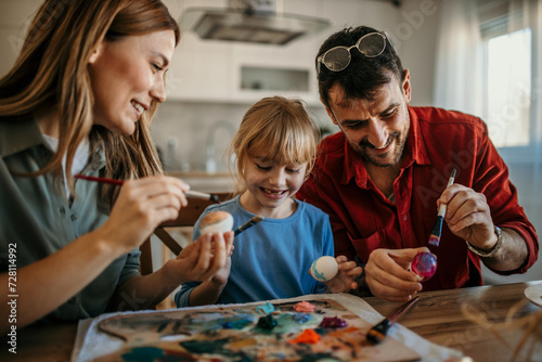 Mom, dad, and child immersed in decorating Easter eggs in the cozy dining room