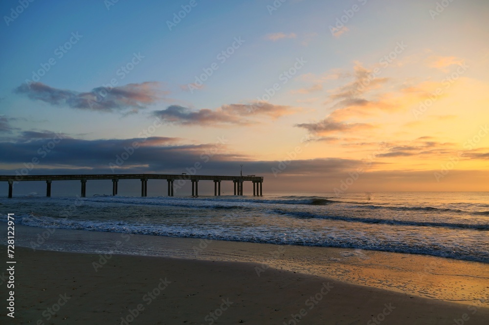 Wooden pier stretching into the Atlantic Ocean from a beach showing both night and day colors
