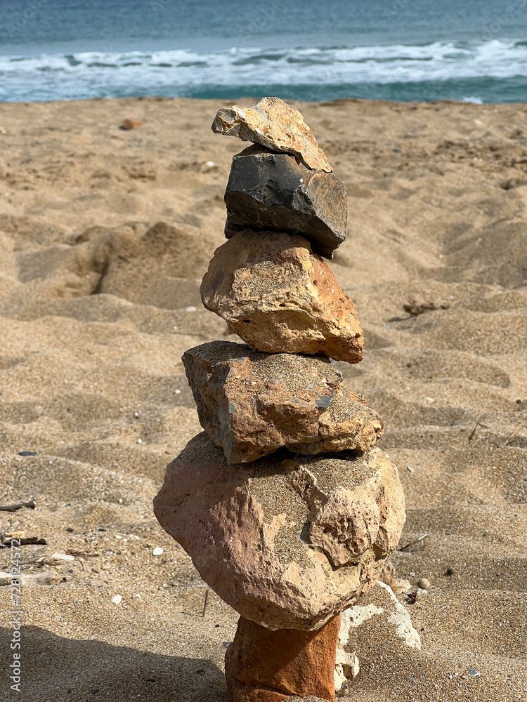 Different sized stones stacked on top of each other in balance on the sandy beach, with the sea in the background