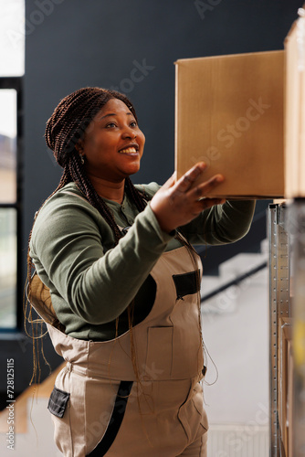 Stockroom worker taking out cardboard box from shelves, preparing customers online orders in warehouse. African american supervisor wearing industrial overall working at products delivery in