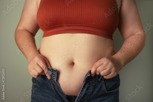 Fat woman trying to zip up her jeans pants. Women's health. Women body fat belly. Obese woman hand holding excessive belly fat. Diet lifestyle concept, healthy stomach muscle.  © Shi 