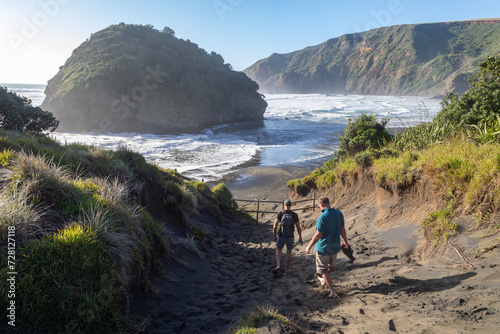 Two people walking down a sand dune looking out to Bethells Beach, Auckland, New Zealand.