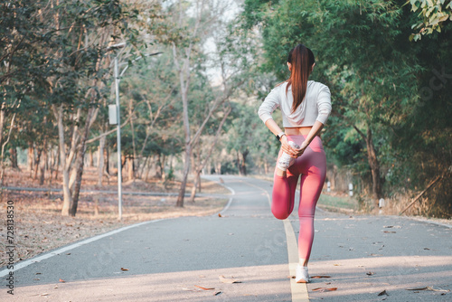 Valokuva Running concept, Rear view of a woman doing a quadriceps stretch on a park path, part of her fitness routine in a natural setting