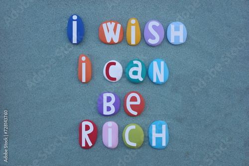 I wish I can be rich, creative text composed with hand painted multi colored stone letters over green sand