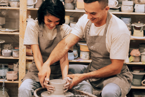 Couple in love working together on potter wheel in craft studio workshop. Lifestyle and hobby concept.