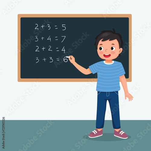 Cute little boy student write on blackboard math equation in front of class with chalk

