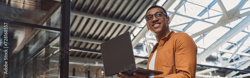 Smiling businessman in casual clothing working on laptop while standing on coworking background