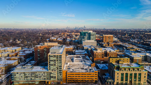 Cityscape: The view captures a panoramic scene of a city during daylight. The architecture consists of modern buildings with varying heights and designs. These structures are adorned with snow-covered