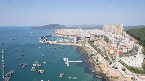 Aerial view of a coastal cityscape with a modern architectural landmark, boats in the bay, and densely packed residential areas on a sunny day