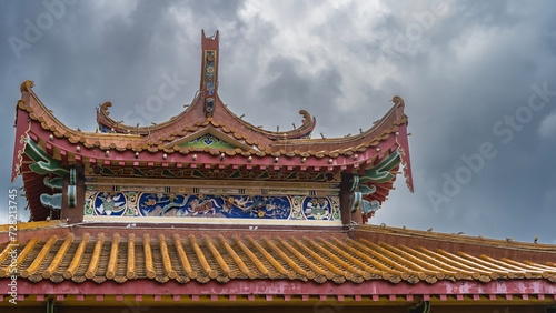 Details of the architecture of the Chinese Thean Hou Temple. The tiled roof with curved edges is decorated with carved ornaments and drawings. The background is a cloudy sky. Malaysia. Kuala Lumpur.