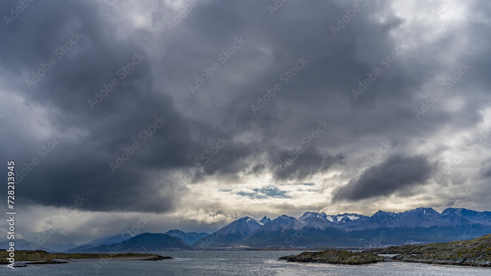 A picturesque mountain range of the Andes against a cloudy sky. In the foreground is the Beagle Channel with rocky islets. Argentina. Patagonia. Tierra del Fuego Archipelago