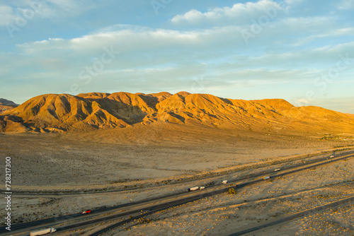 an aerial shot of majestic mountain ranges in the desert at sunset with cars and trucks driving on the highway in Yermo California USA photo
