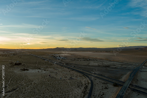 an aerial shot of majestic mountain ranges in the desert at sunset with cars and trucks driving on the highway in Yermo California USA