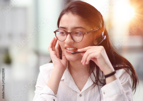 Portrait of a young woman in a headset working in an office center online from a laptop.