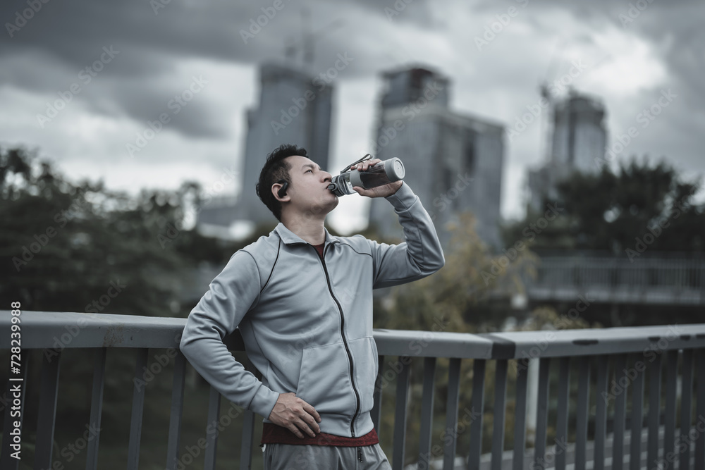Young sport man drink water after jogging, running in the park. Sport thirsty and resting after exercise. Health and Lifestyle in big city life concept. Young sport man drink water after jogging, running in the park. Sport thirsty and resting after exercise. Health and Lifestyle in big city life concept.