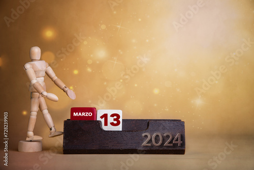 Calendar brilliance in March: Wooden character directs to the thirteenth day amidst a warm-toned, bright background. photo