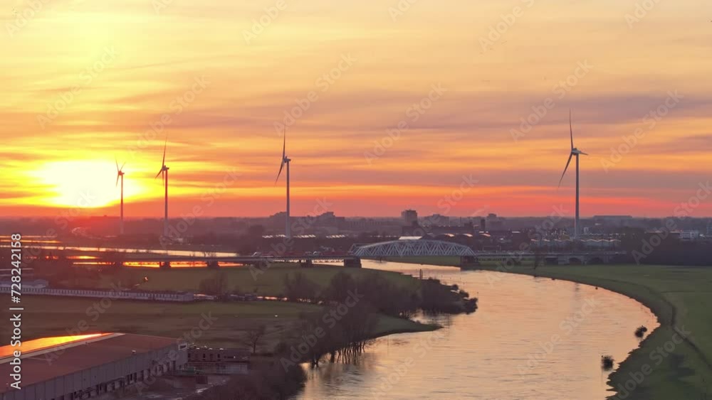 Aerial sunset drone shot passing over the river the IJssel with impressive windturbines and bridge on the horizon. The colors in the sky are impressive and colorfull Aerial sunset drone shot passing over the river the IJssel with impressive windturbines and bridge on the horizon. The colors in the sky are impressive and colorfull