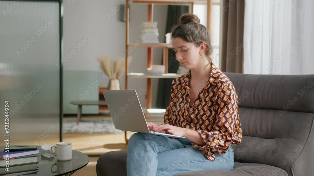 Side view of caucasian woman on couch working-from-home on her laptop on her lap Side view of caucasian woman on couch working-from-home on her laptop on her lap