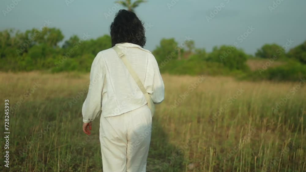 Woman in white walking through a field in daylight, back to camera, serene Woman in white walking through a field in daylight, back to camera, serene
