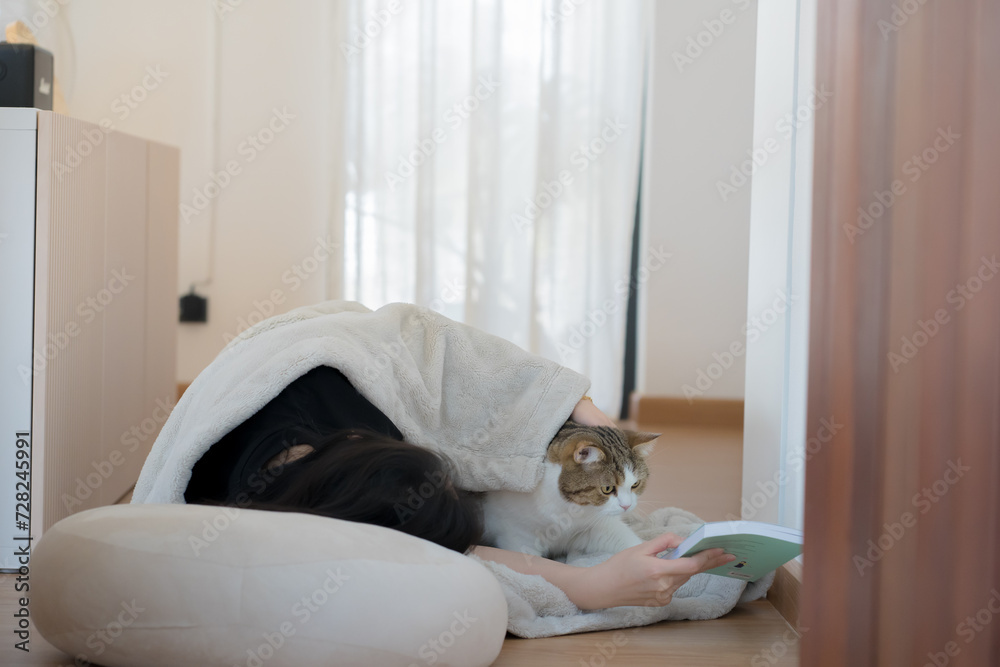 wellness and wellbeing concept with asian woman lie down and read book and play with her cat in livingroom